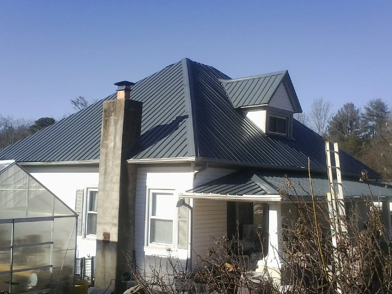 Dark blue standing seam metal roof on a white farmhouse with dormer — Slate & Tile Roof Repair by Roofing Brothers in Big Pool