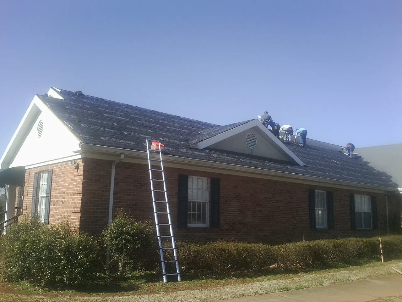 Crew tearing shingles off a brick ranch roof with a ladder set — Emergency Roof Repair work by our crew in Big Pool