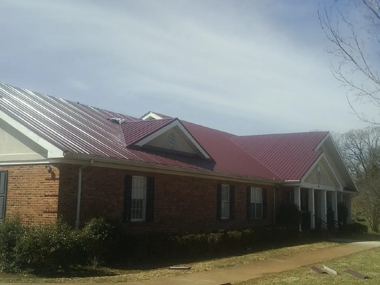Red metal roof with gabled entries on a long brick building, from a Hail Damage Roof Repair job in Big Pool