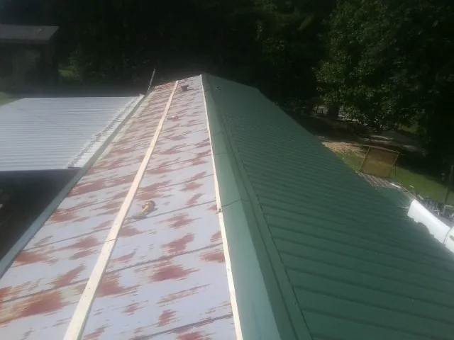 Old rusted panels beside newly installed green metal roofing — Wind Damage Roof Repair by Roofing Brothers in Big Pool
