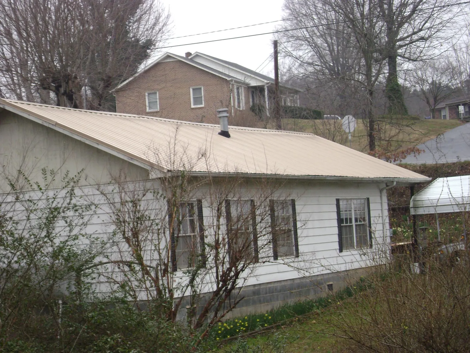 Tan metal roof on a white sided house set into a hillside — Commercial Roofing by Roofing Brothers in Big Pool